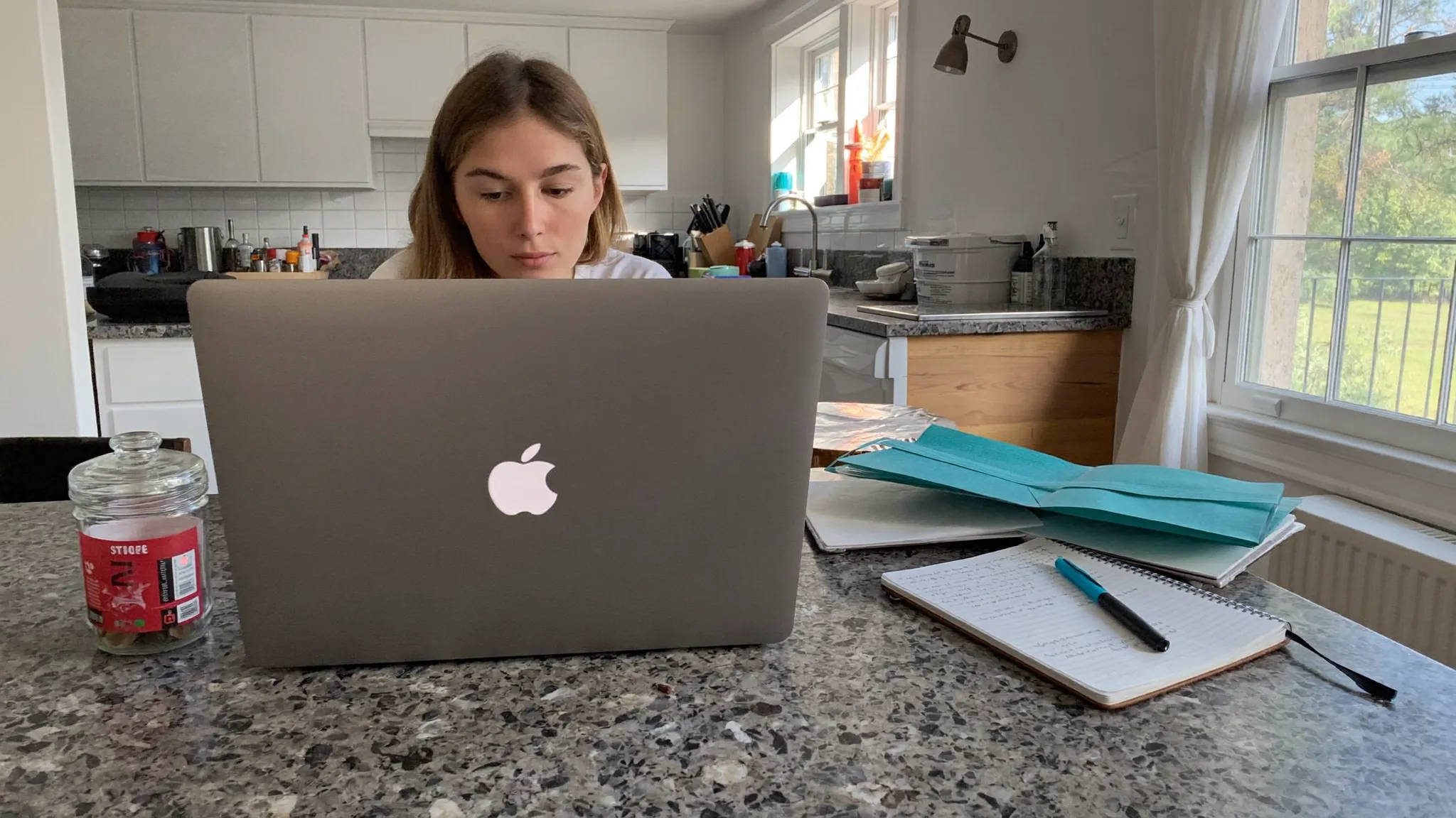 A young couple reviewing a savings plan and budget on a laptop with a jar of coins on the table.